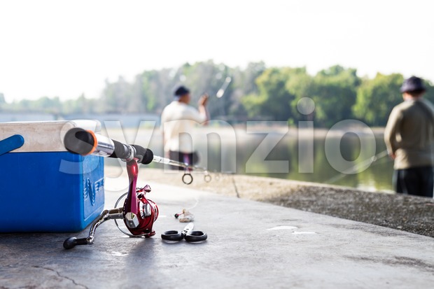 Fishing rod and tool box with anglers having recreation fishing at background Stock Photo