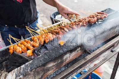 Vendor preparing chicken and beef barbecue satay on charcoal grille Stock Photo