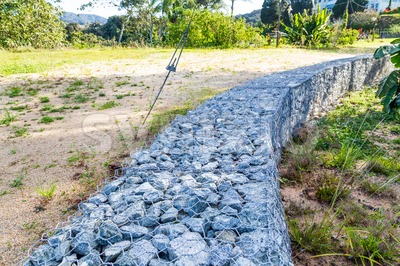 Slope earth retention wall with rocks and wire mesh cage Stock Photo