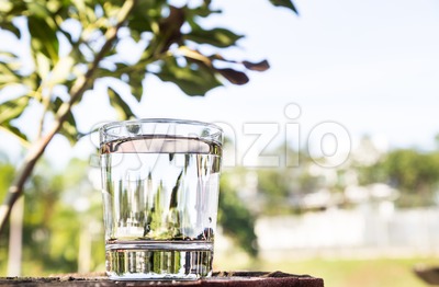 Refreshing water in transparent glass  against blue sky and greenaries Stock Photo