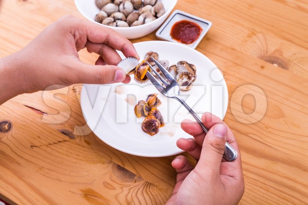 Person extracting cockles from its shell for consumption with dips Stock Photo