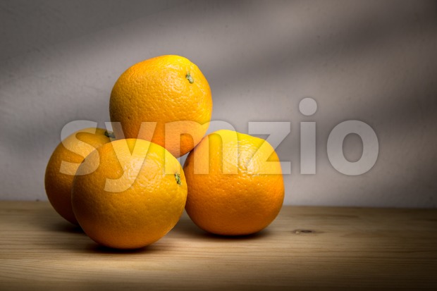Four fresh oranges on wooden table with rays of light Stock Photo