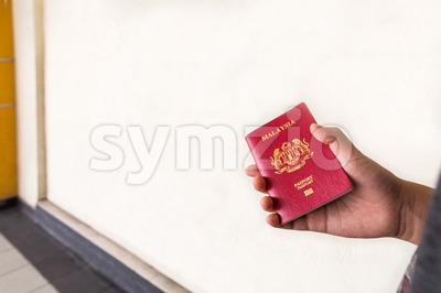 Hand holding Malaysia international passport against wall background Stock Photo