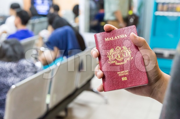 Hand holding Malaysia international  passport against bokeh crowd background Stock Photo