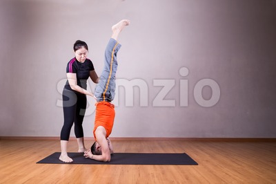Yoga instructor guiding student perform head stand pose or Sirsasana Stock Photo