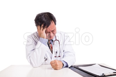 Depressed sad matured Asian doctor seated behind desk Stock Photo