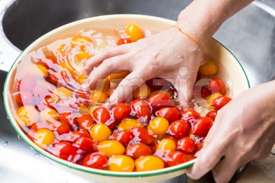 Hand washing cherry tomato with running water in household sink Stock Photo