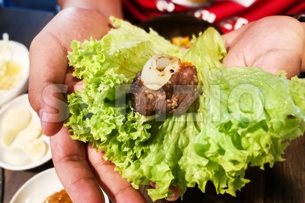 Hand holding korean barbecue beef and garlic wrap with salad Stock Photo