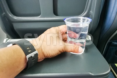 Hand holding disposable mineral water on table in air plane Stock Photo