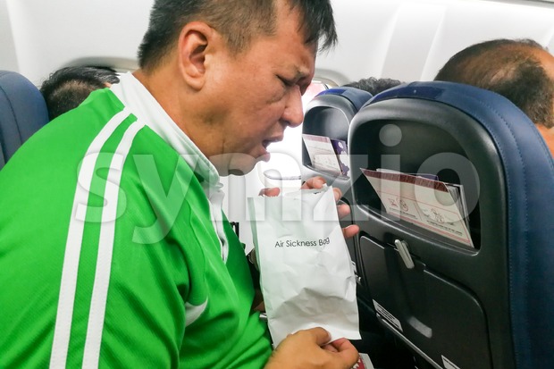 Nauseous air sickness Asian man vomiting into air sickness bag Stock Photo