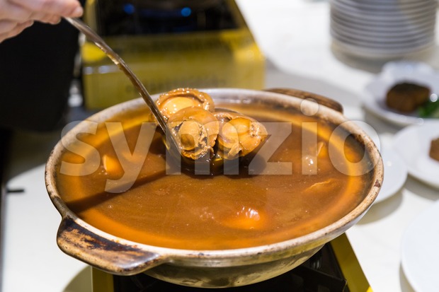 Delicious braised abalone scooped out from ceramic pot for serving Stock Photo