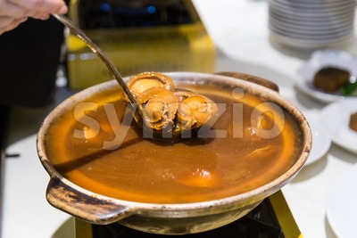 Delicious braised abalone scooped out from ceramic pot for serving Stock Photo