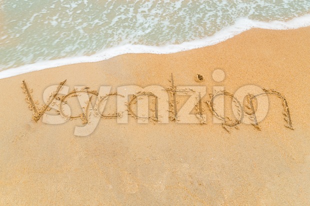 VACATION inscription written on sandy beach with wave approaching Stock Photo