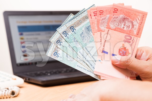 Hand holding Malaysia Ringgit in office with computer in background Stock Photo