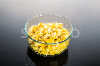 Corn kernels in transparent glass bowl in dark background Stock Photo