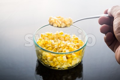 Selective focus on spoonful of corn kernels against dark background Stock Photo