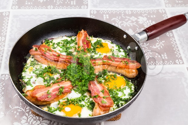 Delicious bacon strips, sausages and fried eggs breakfast in pan. Stock Photo